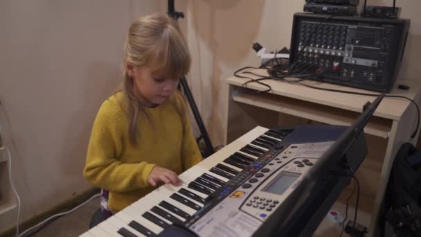Маленькая девочка за электронным фортепиано учится играть мелодию. — стоковое видео