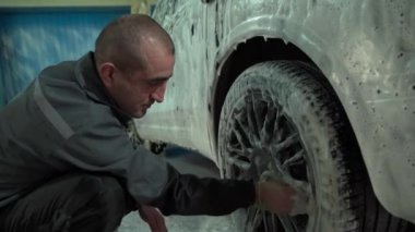 Beyaz bir adam araba yıkamada çalışır. Bir araba yıkama işçisi arabayı yıkar. Servis çalışanı arabanın direksiyonunu yıkar..