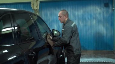 Beyaz bir adam araba yıkamada çalışır. Bir araba yıkama işçisi arabayı yıkar. Servis çalışanı arabayı paçavrayla siler.