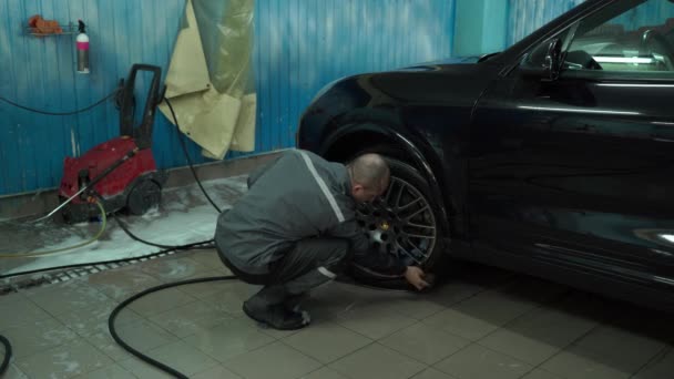 Een blanke man werkt in een wasstraat, een wasstraat wast de auto. De servicemedewerker veegt de auto af met een doek — Stockvideo