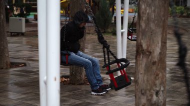 Parkta sallanan yalnız bir adam. Bunalımda olan üzgün bir adam ıssız bir kış parkında salıncakta sallanıyor..