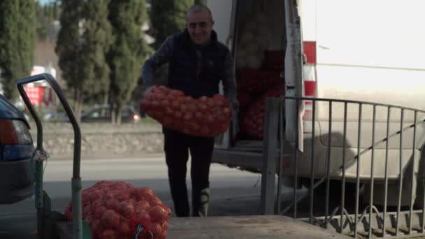 Ein kaukasischer Mann lädt große Säcke Zwiebeln auf einen Wagen. — Stockvideo