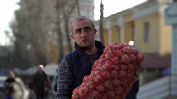 Porträt eines kaukasischen Arbeiters, der eine schwere Tasche mit Zwiebeln in der Hand hält — Stockvideo