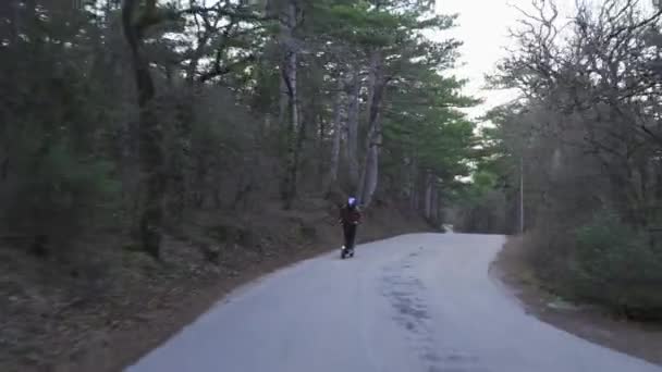 Seorang pengemudi memakai helm pelindung dan skuter listrik yang kuat berkendara di sepanjang jalan hutan. Seorang pria mengendarai skuter listrik di hutan di jalan beton mengikuti kamera. — Stok Video