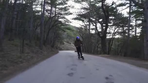 Un conducteur portant un casque de protection et un scooter électrique puissant conduit le long d'une route forestière. Un homme sur un scooter électrique dans la forêt balade le long de la route — Video