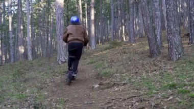 Koruyucu kask takan ve güçlü bir elektrikli scooter kullanan bir sürücü orman yolunda araba sürer. Elektrikli scooter kullanan bir adam ormanda orman yollarında geziyor.
