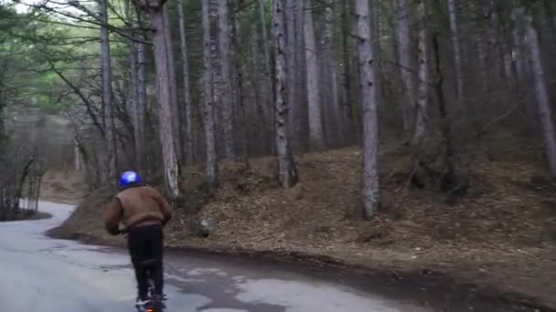 Ein Fahrer mit Schutzhelm und einem leistungsstarken Elektroroller fährt einen Waldweg entlang. Ein Mann auf einem Elektroroller fährt eine lange Strecke im Wald entlang der Straße mit dem Rücken zur Wand. — Stockvideo