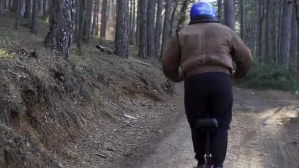保護ヘルメットと強力な電動スクーターを身に着けているドライバは、森林道に沿って駆動します。道路沿いの森の中を電動スクーターで走っている男 — ストック動画