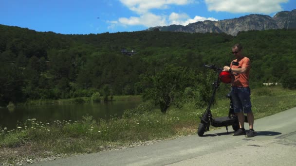 Езда на мощном электромобиле. Мужчина подходит к мощному электрическому скутеру, надевает защитный шлем и едет вперед на фоне зеленого леса.. — стоковое видео