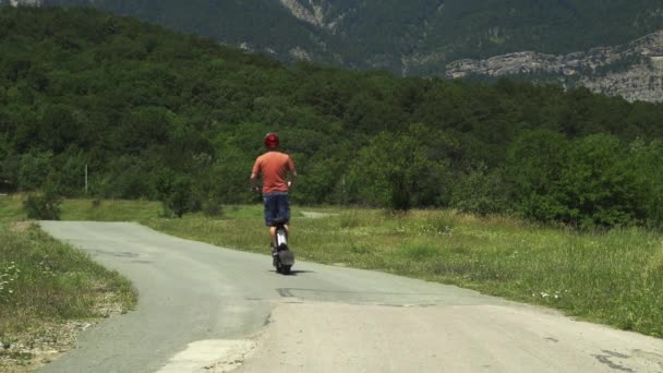 Montar un poderoso vehículo eléctrico. Un hombre en un casco protector cabalga a lo largo de un camino forestal en un scooter eléctrico desde la cámara. — Vídeos de Stock