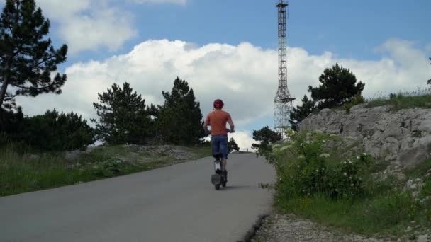 Güçlü bir elektrikli araca binmek. Elektrikli scooterlı koruyucu kasklı bir adam eski bir demir kulenin arka planına doğru yola çıkıyor. — Stok video