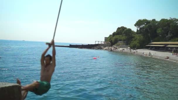 Un joven en un bungee balanceándose y saltando al mar haciendo volteretas. — Vídeo de stock