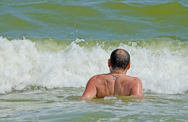 Un hombre nada en el mar y mira la gran ola marina espumosa — Foto de Stock