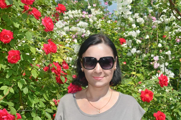 Mooie brunette vrouw in de struiken roos en jasmijn bloemen — Stockfoto