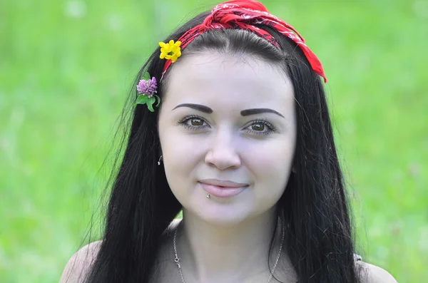 Retrato de una joven, hermosa, morena con flores en el pelo y bufanda. En el contexto de la hierba verde — Foto de Stock