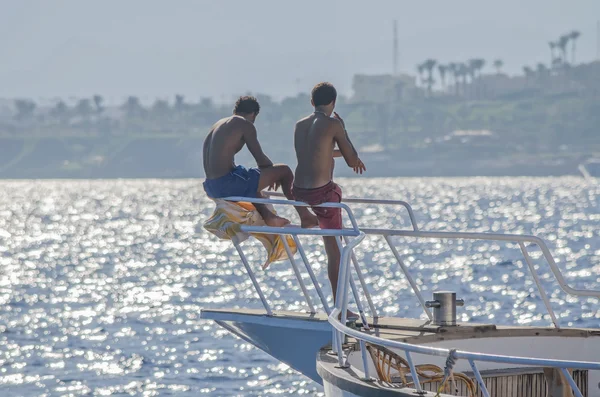 Egito, Mar Vermelho. Dois homens egípcios sentam-se no nariz e olham para os barcos em terra . — Fotografia de Stock