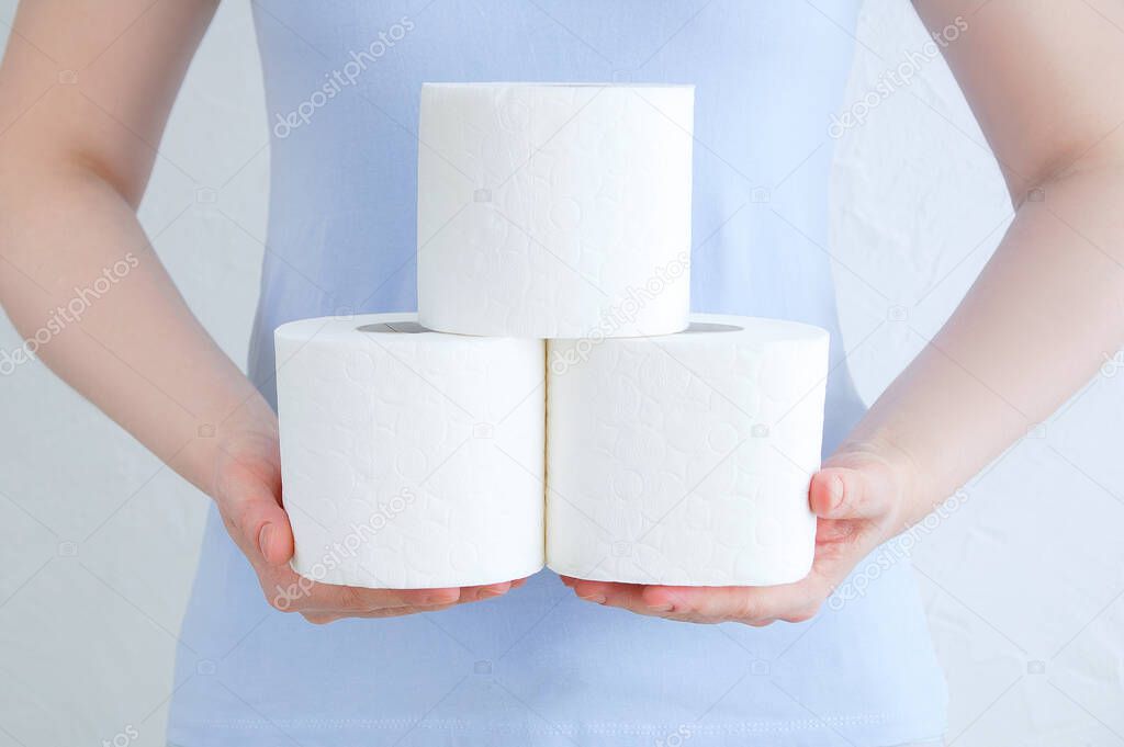 Rolls of toilet paper in the hands of a Caucasian woman against the background of a white wall.