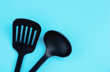 Yemek pişirmek için mutfak aletleri. Turkuaz arka planda siyah plastik kepçeler.