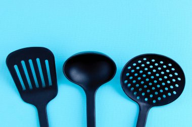 Yemek pişirmek için mutfak aletleri. Turkuaz arka planda siyah plastik kepçe, spatula ve kepçe..