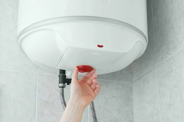 Banyodaki duvardaki beyaz elektrikli su ısıtıcısının ısısını ayarlıyorum..