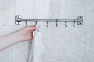 Banyodaki metal askıya beyaz bir havlu asıyor..