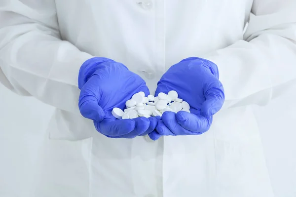 A handful of white pills on the palms of a hand in medical gloves close-up.