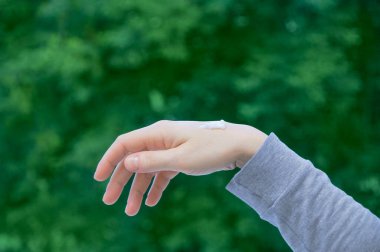 Beyaz bir kadının elindeki bir damla el kremi yeşil yapraklı bir arka plana karşı. Doğal cilt bakımı kavramı.