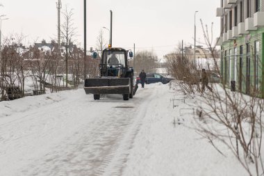Moskova. - Rusya. Kış 2021. Küçük bir traktör evin yakınındaki yoldan karları temizliyor..