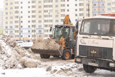 Moskova. - Rusya. Kış 2021. Büyük bir traktör arabayı çok katlı binaların bahçelerine karla dolduruyor..