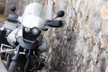 Taş duvarda off-road motosikleti. Duvara yaslanmış gri bir motosiklet var..