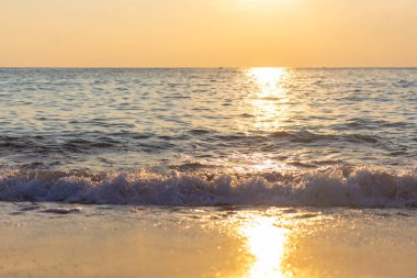 Alçak güneşten sarı gün batımı. Dalgaların üzerinde gün batımı yolu olan bir sahil..