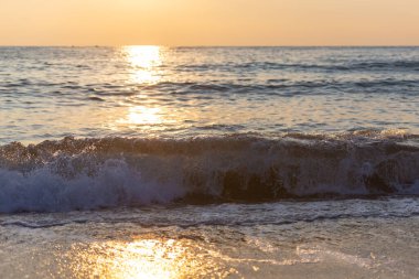 Alçak güneşten sarı gün batımı. Dalgaların üzerinde gün batımı yolu olan bir sahil..
