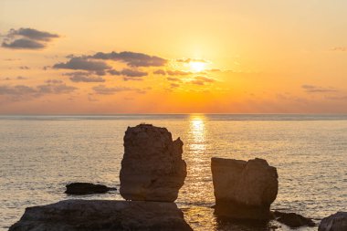 Gün batımı, kayaların arasında, denizde güneşli bir yol çizer..