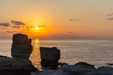 Gün batımı, kayaların arasında, denizde güneşli bir yol çizer..