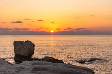 Gün batımı, kayaların arasında, denizde güneşli bir yol çizer..
