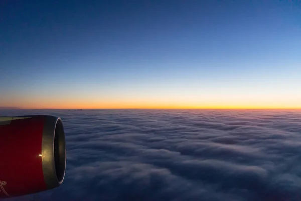 Photo from the window of the plane. We meet the dawn in the sky. Dense clouds and an airplane engine.