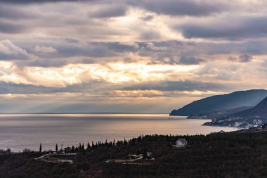 Kırım 'ın güney sahillerinde kışın günbatımında. Güneşin gün batımı ışınları bulutları delip geçiyor. Dağlar, sahil ve güzel manzaralar.