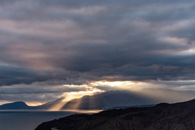 Kırım 'ın güney sahillerinde kışın günbatımında. Güneşin gün batımı ışınları bulutları delip geçiyor. Dağlar, sahil ve güzel manzaralar.