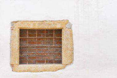 Pencere tuğla ve parmaklıklarla örülmüş. Beyaz duvarda parmaklıklı bir pencere var..