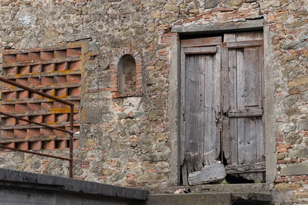 The wall of an old stone barn. An old and decayed wooden door in an old barn in Tuscany.