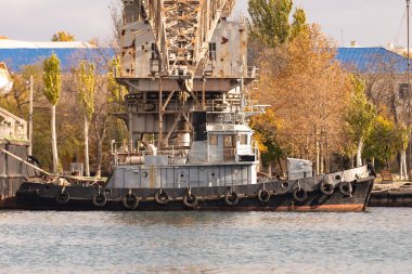 Sivastopol. Kırım. Kış 2021. Gemi, vincin önündeki rıhtımın duvarını çekiyor. Yanı lastikli siyah-gri bir römorkör iskeleye paralel demirlenmiş..