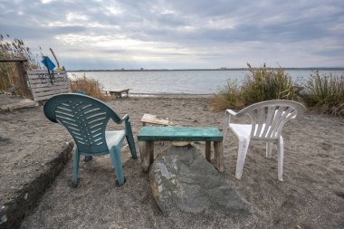 Bulgaristan 'ın Burgaz bölgesinin Pomorie kenti yakınlarındaki Pomorie tuz gölünde plastik sandalyeler ve masa. Deniz tuzu üretimi