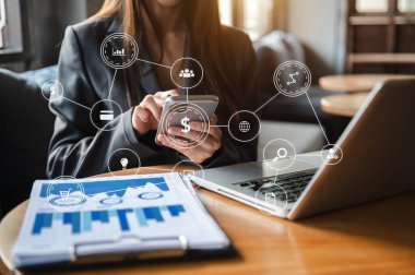 İş kadını el bilgisayarı cep telefonuyla sanal ekranda dijital pazarlama medyasında çalışıyor ve sabah saatlerinde ofiste VR simgesi diyagramı ile modern hesaplama yapıyor.