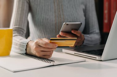  Mobil ödemeler için akıllı telefon kullanan bir kadın çevrimiçi alışveriş, Omni kanalı, masada oturan, sabah ışıklarında sanal simge grafik arayüzü ekranı