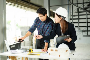 İki genç Asyalı mimar inşaat planlarını dizüstü bilgisayarla, ölçekli modelle ve inşaat alanında tartışıyorlar. Takım çalışması, yaratıcılık ve kentsel gelişim kavramı