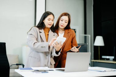 Gülümseyen Asyalı iş kadınları modern bir ofiste tablet ve dizüstü bilgisayar üzerinde işbirliği yaparak strateji ve analizi tartışıyor. Takım çalışması, planlama ve iş kavramları için mükemmel.