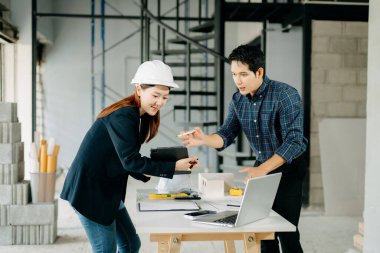 İki genç Asyalı mimar inşaat planlarını dizüstü bilgisayarla, ölçekli modelle ve inşaat alanında tartışıyorlar. Takım çalışması, yaratıcılık ve kentsel gelişim kavramı
