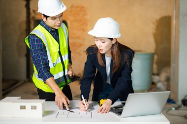 Katı şapkalı inşaat uzmanları, tablet ve pano ile bina tasarımı, planlama ve güvenlik alanlarında işbirliği yaparak, çalışma tablosu ve ölçekli bir modelin planlarını ve ölçekli modelini inceliyorlar..