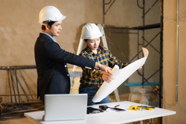 Asyalı mimarlar ve mühendisler modern ofis sitesinde planlar, dizüstü bilgisayarlar ve takım çalışması ile inşaat projesi yapmayı planlıyorlar. Mimarlık ve inşaat konsepti için mükemmel