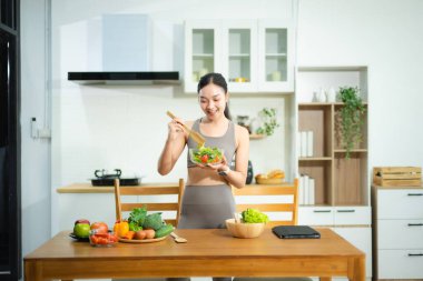 Gülümseyen Asyalı kadın ev mutfağında taze sebze salatası hazırlıyor. Sağlıklı yaşam tarzı, temiz yemek, sağIık ve zindelik gıda hazırlık konsepti..